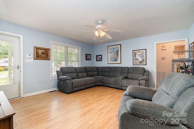 living area featuring baseboards, a ceiling fan, light wood-style flooring, and a wealth of natural light