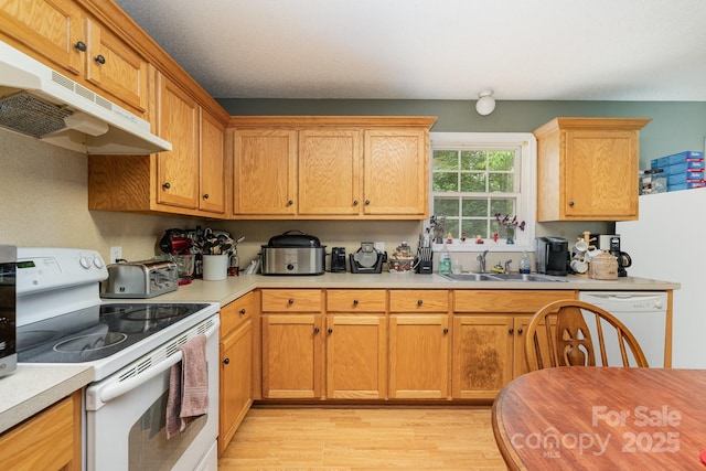 kitchen featuring a sink, white appliances, light countertops, light wood-style flooring, and under cabinet range hood