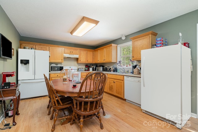 kitchen featuring light countertops, a sink, light wood finished floors, under cabinet range hood, and white appliances