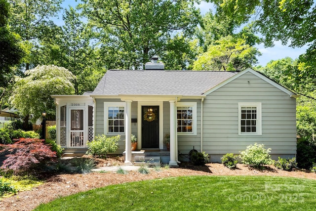 view of front of house featuring roof with shingles, a chimney, and a front lawn