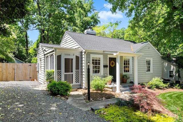 bungalow-style home with fence, a chimney, and a shingled roof