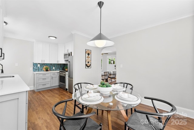 dining area featuring crown molding, arched walkways, baseboards, and light wood-type flooring