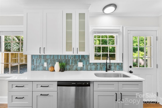 kitchen with light countertops, glass insert cabinets, a sink, and dishwasher