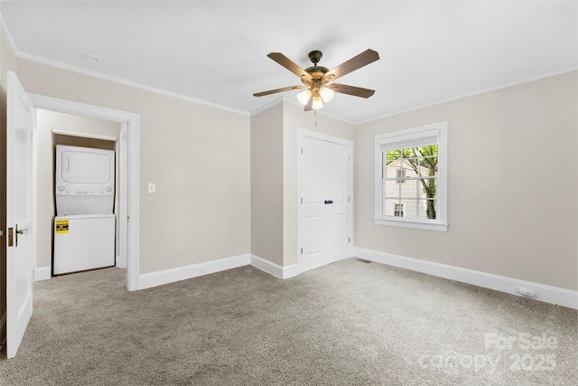 carpeted empty room featuring crown molding, baseboards, and stacked washing maching and dryer