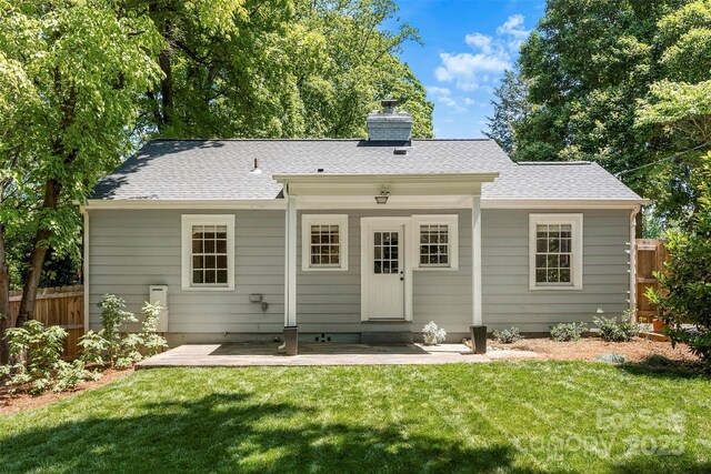 rear view of property with a shingled roof, fence, a yard, and a chimney