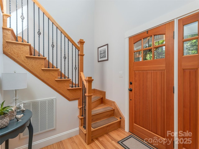 foyer featuring stairway, baseboards, wood finished floors, and visible vents