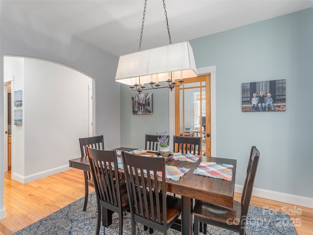 dining space featuring baseboards, arched walkways, light wood finished floors, and a notable chandelier