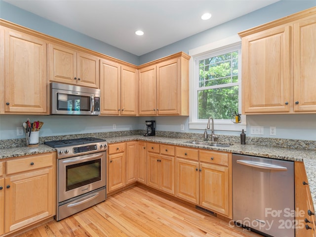 kitchen with light brown cabinetry, light stone counters, appliances with stainless steel finishes, a sink, and light wood-type flooring