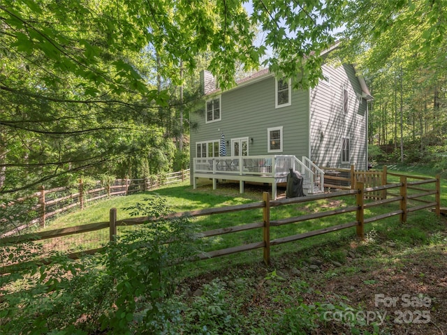 rear view of property with a fenced backyard, a wooden deck, a chimney, and a yard