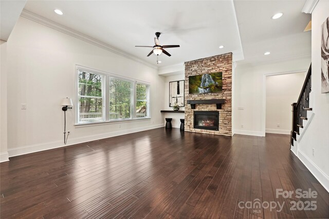 unfurnished living room featuring ceiling fan, a stone fireplace, wood finished floors, ornamental molding, and stairs