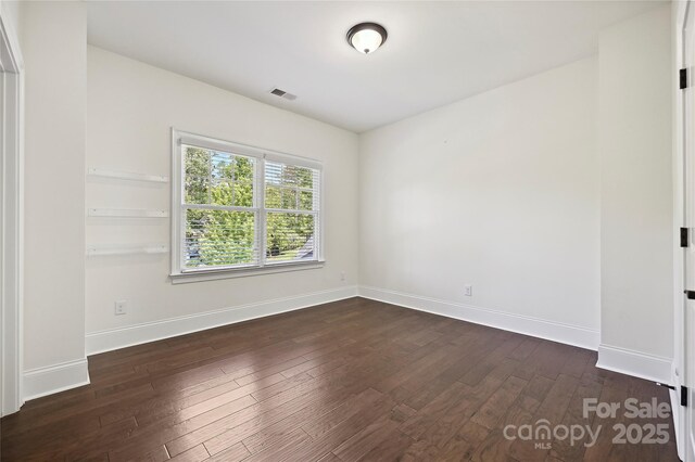 spare room with baseboards, dark wood-style floors, and visible vents