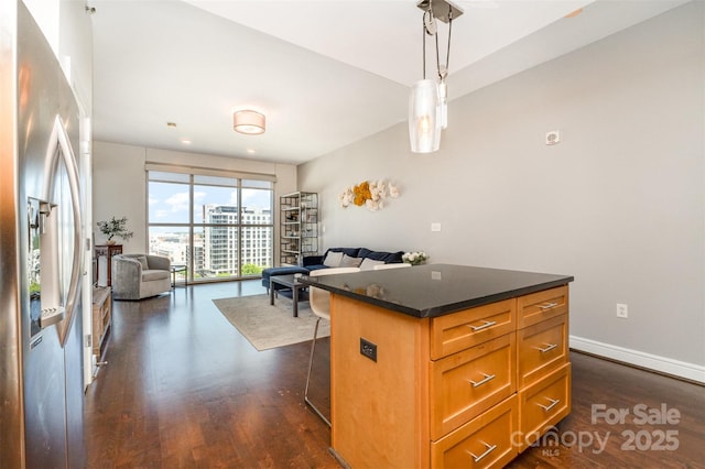 kitchen with a breakfast bar area, dark countertops, dark wood-style floors, open floor plan, and stainless steel fridge