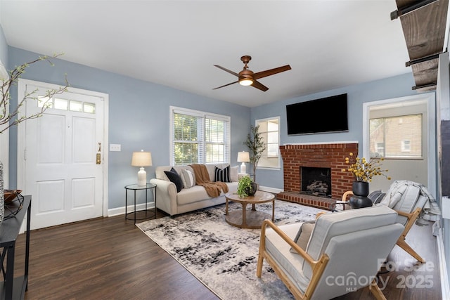 living area featuring baseboards, a ceiling fan, a brick fireplace, and wood finished floors