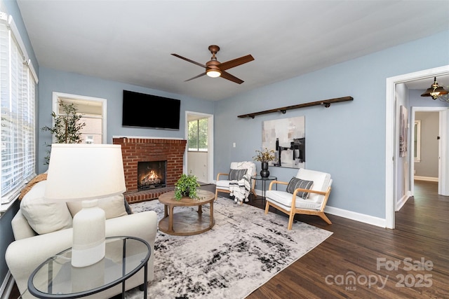 living room with baseboards, a ceiling fan, a brick fireplace, and wood finished floors