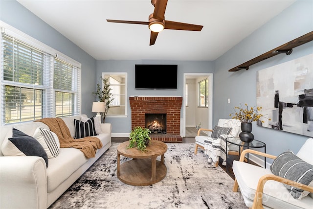 living room featuring baseboards, a brick fireplace, ceiling fan, and wood finished floors