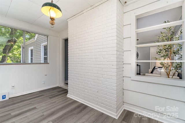 spare room featuring brick wall, baseboards, and wood finished floors