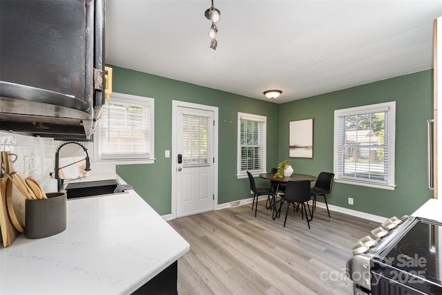 kitchen with baseboards, light countertops, a sink, light wood-style flooring, and stainless steel range with electric cooktop