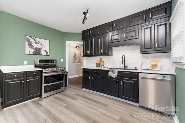 kitchen with a sink, light countertops, dark cabinets, stainless steel appliances, and light wood-type flooring