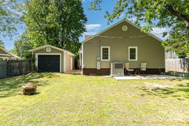 back of property with a lawn, an outbuilding, a detached garage, fence, and a fire pit
