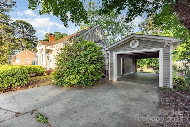 exterior space featuring driveway, a chimney, an outdoor structure, and a garage