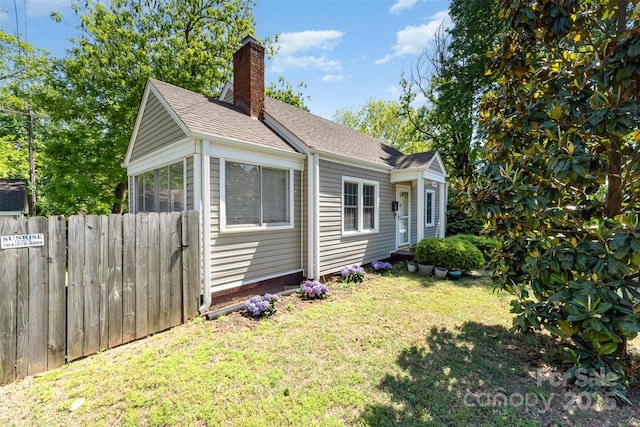 exterior space featuring a yard, fence, a chimney, and roof with shingles