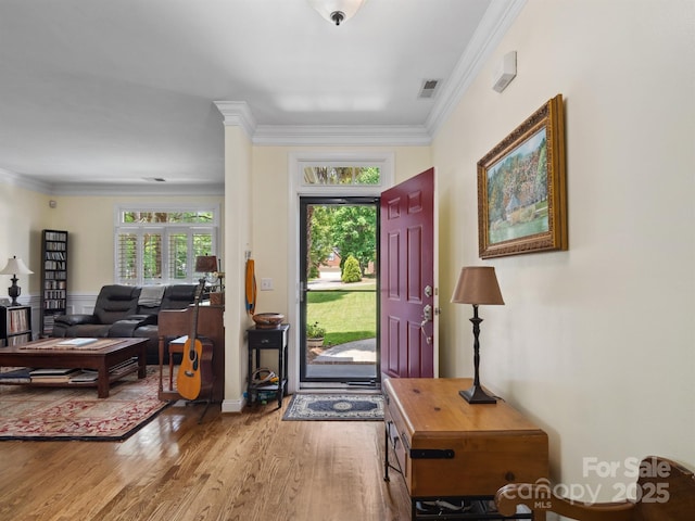 entryway with a wealth of natural light, ornamental molding, wood finished floors, and visible vents