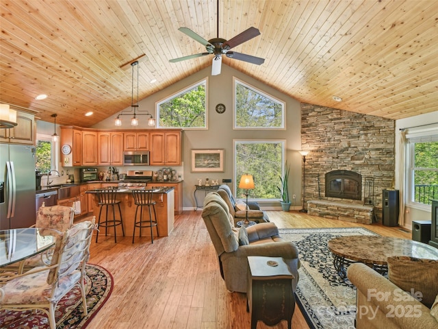 living area featuring wood ceiling, ceiling fan, a stone fireplace, high vaulted ceiling, and light wood finished floors