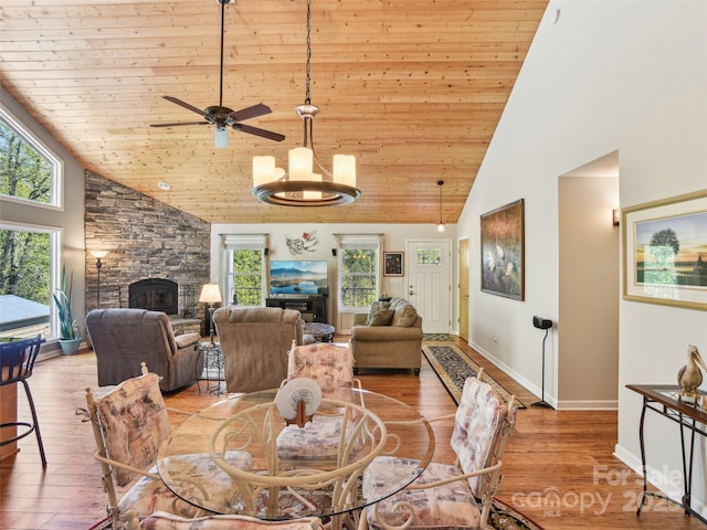 dining room with a stone fireplace, wood finished floors, high vaulted ceiling, and wooden ceiling