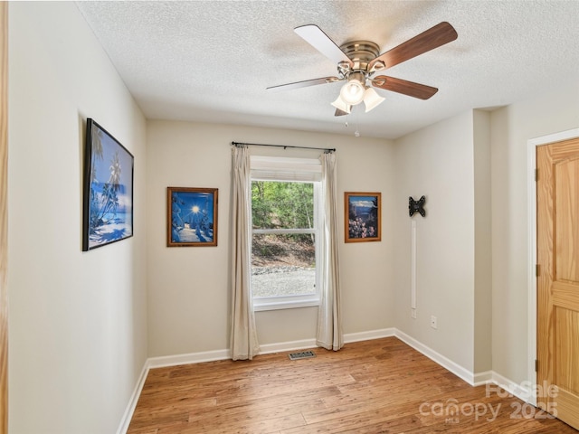 empty room featuring a ceiling fan, a textured ceiling, baseboards, and light wood-style floors
