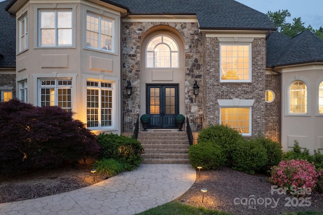 view of exterior entry with french doors, a shingled roof, and stone siding
