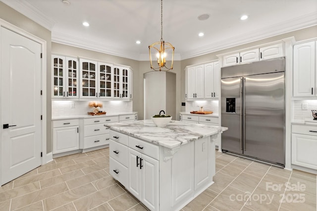 kitchen with an inviting chandelier, a center island, stainless steel built in refrigerator, tasteful backsplash, and glass insert cabinets