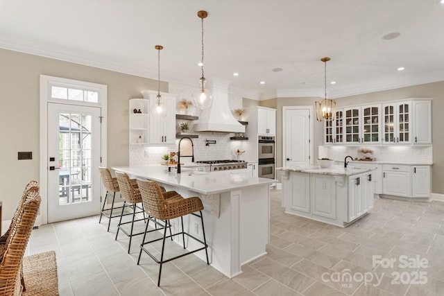 kitchen with stainless steel double oven, a breakfast bar area, premium range hood, white cabinetry, and tasteful backsplash