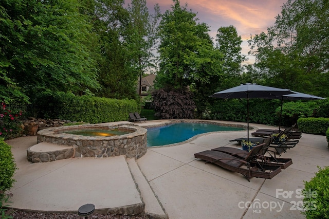 pool at dusk with a patio and a pool with connected hot tub