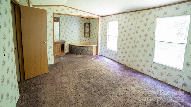 spare room featuring a healthy amount of sunlight, carpet, vaulted ceiling, and wallpapered walls