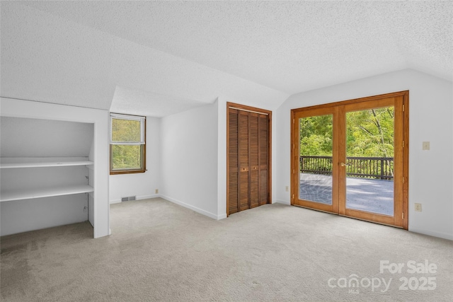 unfurnished bedroom featuring vaulted ceiling, carpet flooring, a textured ceiling, and access to exterior