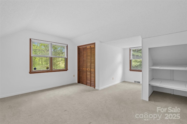 bonus room featuring carpet floors, visible vents, lofted ceiling, a healthy amount of sunlight, and a textured ceiling