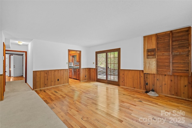empty room with light wood-style floors, wainscoting, and wood walls