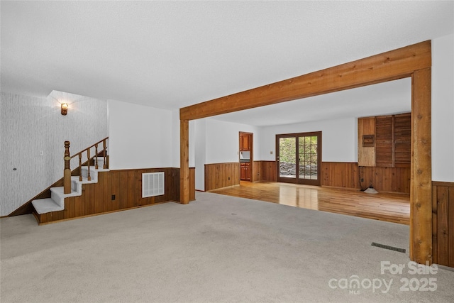 carpeted spare room with wooden walls, a wainscoted wall, stairs, and visible vents