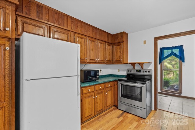 kitchen featuring brown cabinetry, freestanding refrigerator, black microwave, and stainless steel electric range oven