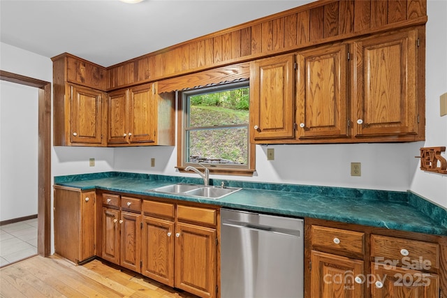 kitchen with stainless steel dishwasher, brown cabinets, dark countertops, and a sink