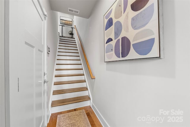 stairway with baseboards, visible vents, and wood finished floors