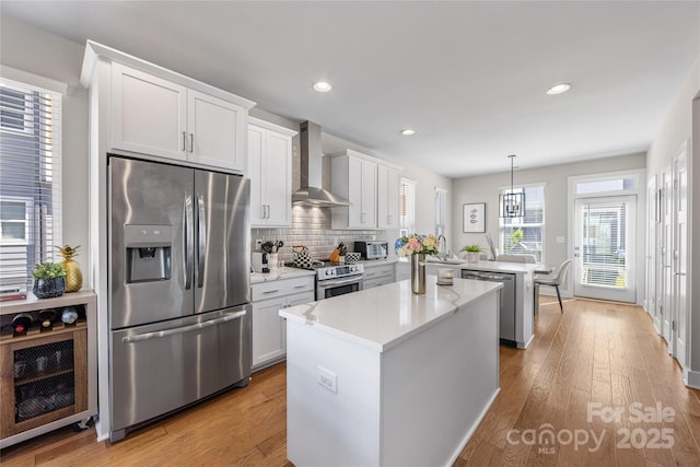 kitchen featuring wall chimney range hood, a center island, a peninsula, light wood-style floors, and stainless steel appliances