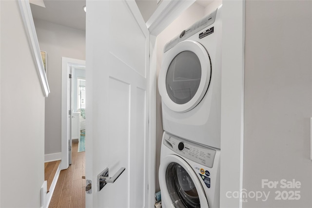 clothes washing area featuring wood finished floors, laundry area, baseboards, and stacked washer / drying machine