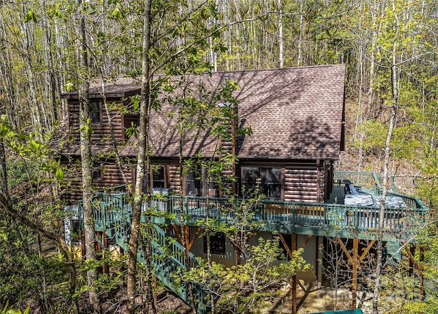 rear view of property featuring a deck, roof with shingles, faux log siding, and a view of trees