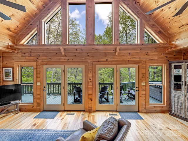 doorway to outside with wood-type flooring, plenty of natural light, wooden walls, a ceiling fan, and high vaulted ceiling