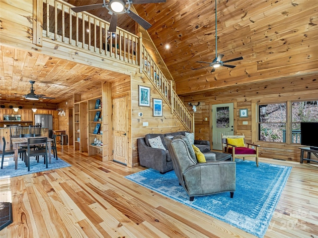 living room with a ceiling fan, stairway, wooden walls, light wood-style flooring, and wooden ceiling