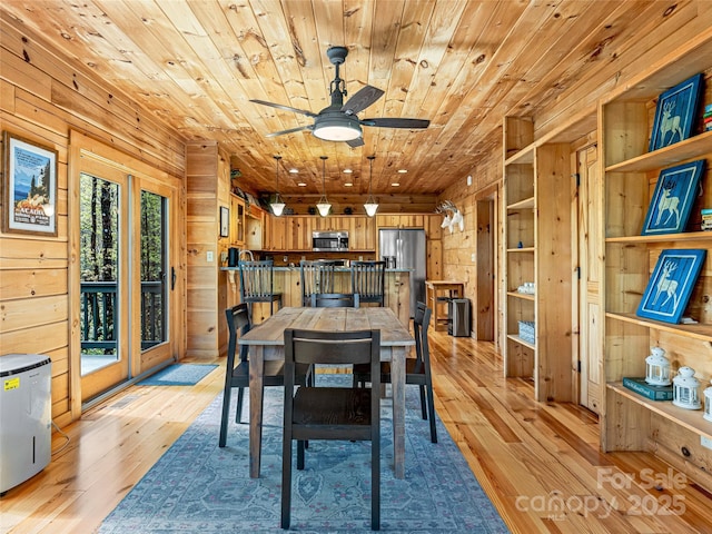 dining room with wooden walls, wood ceiling, light wood-type flooring, and a ceiling fan