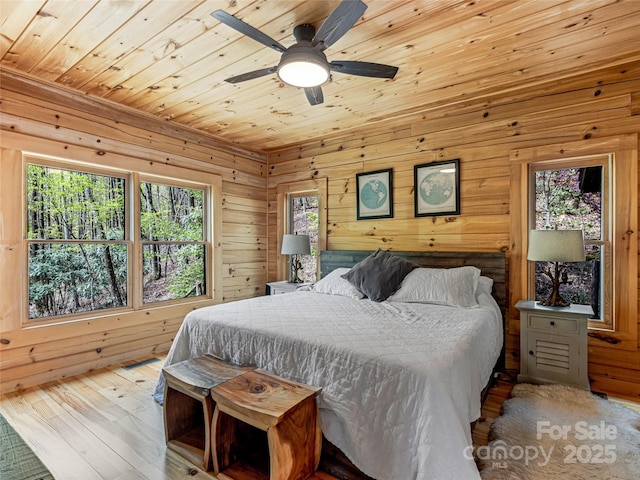 bedroom with multiple windows, wood ceiling, wooden walls, hardwood / wood-style floors, and ceiling fan