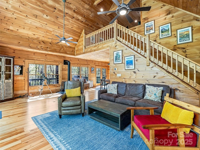living room with a ceiling fan, wood walls, high vaulted ceiling, stairs, and hardwood / wood-style floors