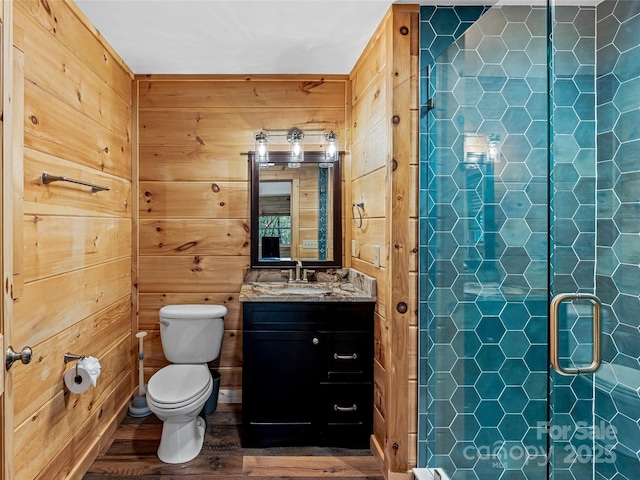 bathroom featuring wood finished floors, a shower stall, toilet, vanity, and wooden walls